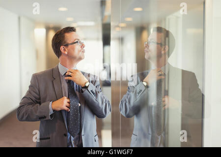 La riflessione di fiduciosa imprenditore tirante di regolazione nel corridoio di office Foto Stock