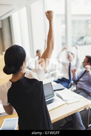 Esuberante imprenditrice gesticolando con pugno e di celebrare con i colleghi in sala conferenze Foto Stock