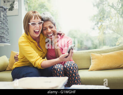 Ridere donne mature abbracciando e tenendo selfie sul divano Foto Stock