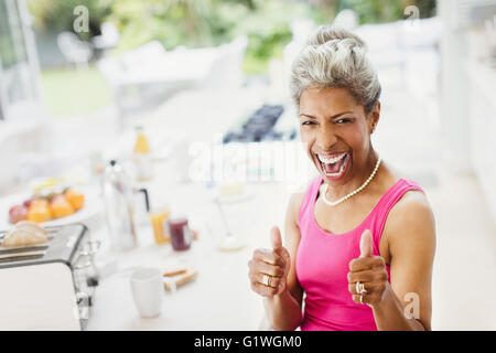 Ritratto entusiastico fiducioso donne mature gesticolando pollice in su in cucina Foto Stock
