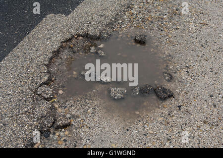 Asfalto con buche riempite con acqua e pezzi di asfalto Foto Stock