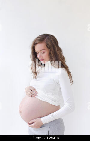 Donna incinta ad accarezzarle il ventre su bianco Foto Stock