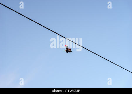 Vecchio paio di scarpe appeso sul filo telefonico contro il cielo blu, vita concetto di modifica Foto Stock