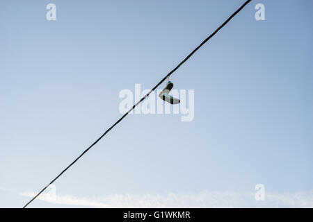 Vecchio paio di scarpe da ginnastica penzolante sulla linea di alimentazione cavo contro il cielo blu, vita concetto di modifica Foto Stock