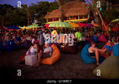 Western villeggiante gustando un drink sulla spiaggia mentre osservate il sole tramontare sull'isola di Bali in Indonesia bevendo un cocktail. Foto Stock