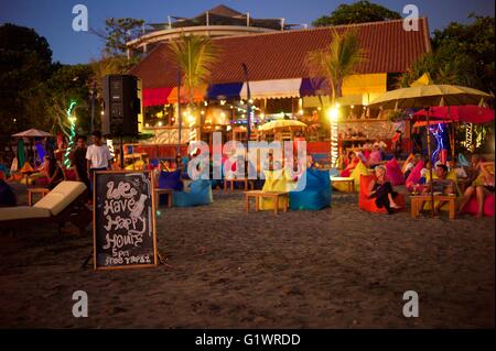 Western villeggiante gustando un drink sulla spiaggia mentre osservate il sole tramontare sull'isola di Bali in Indonesia. Foto Stock