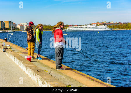 Karlskrona, Svezia - 3 Maggio 2016: tre giovani adulti in piedi procedure Dockside Wizard. Uno è la pesca dopo l'aringa. Due hanno dreadlocks uno ha Foto Stock