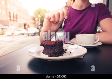Una giovane donna è un caffè e una fetta di torta al di fuori dalla strada Foto Stock