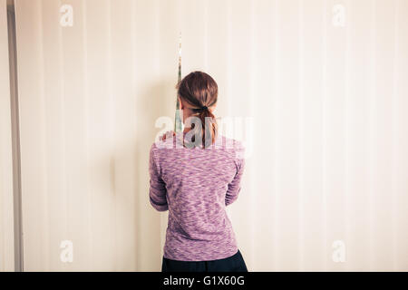 Una giovane donna è in piedi dalle persiane di un pavimento a finestra sul soffitto Foto Stock