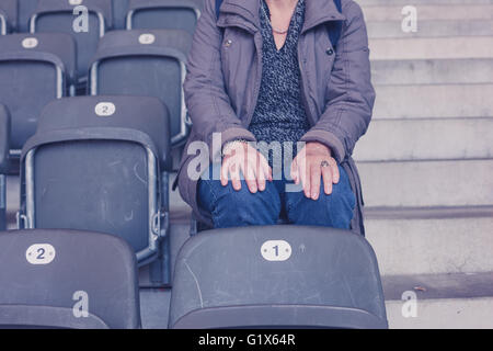 Una donna anziana è seduta sulle gradinate in uno stadio vuoto Foto Stock