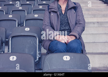 Una donna anziana è seduta sulle gradinate in uno stadio vuoto Foto Stock