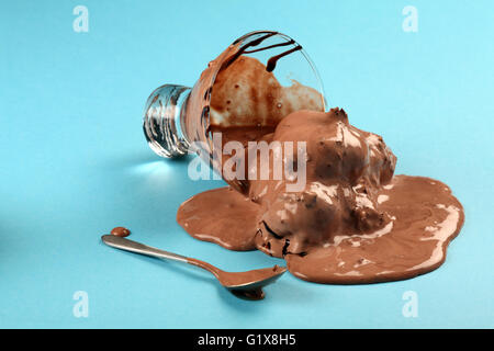 Foto di una tazza di cioccolato fondente gelati ribaltato e fusione attraverso una tabella blu. Foto Stock