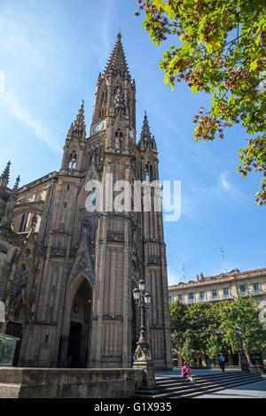 Ornately scolpito torre della cattedrale di Buen Pastor, San Sebastian, Spagna contro un cielo blu con un albero in foglia in primo piano Foto Stock