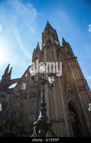 Luce posteriore ornato triplo standard lampada con la torre di orologio della Cattedrale di Buen Pastor, San Sebastian, Spagna sullo sfondo di un cielo blu Foto Stock