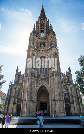 Facciata ornata della torre di orologio della Cattedrale di Buen Pastor, San Sebastian, Spagna contro un cielo blu e turisti in primo piano Foto Stock