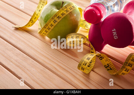 Green manubri, apple e nastro di misurazione su pavimento di legno per le donne. Concetto la salute, la dieta e sport. Composizione orizzontale. Foto Stock