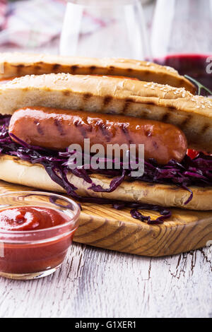 Salsicce alla griglia in sandwich con cavoli rossi dolci coleslaw, la senape e la salsa di pomodoro sulla tavola di legno Foto Stock