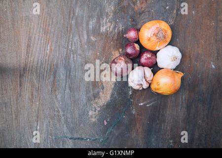 Immagine morbida di cipolle rosse, cipolle, aglio e mortaio di pietra sul vecchio di legno. Messa a fuoco selettiva con profondità di campo ridotta. Foto Stock