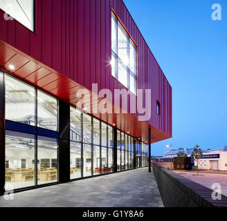Vista lungo piano terra vetri e rosso in acciaio con rivestimento interni illuminati. Plymouth Creative School of Art di Plymouth, Regno Unito. Architetto: Feilden Clegg Bradley Studios LLP, 2015. Foto Stock