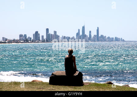 Donna seduta su roccia guardando attraverso il alti edifici della Gold Coast di Queensland in Australia Foto Stock