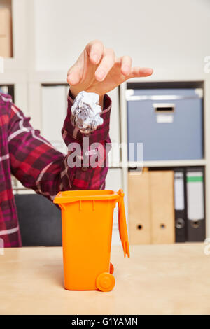 La mano di gettare carta sgualcita in un piccolo cestino Foto Stock