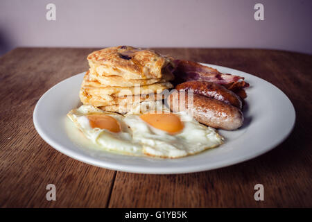 Una colazione con pila corta di frittelle, uova con pancetta e salsicce Foto Stock