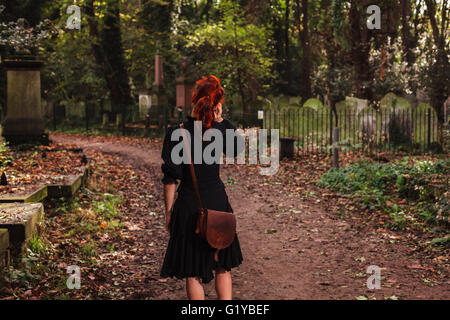 Una donna sta camminando in un cimitero e sta parlando al telefono Foto Stock