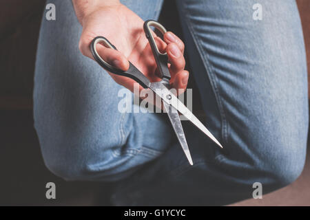 Un uomo è seduto ed è in possesso di forbici Foto Stock