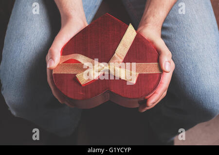 Un uomo è seduto e tenendo un cuore scatola sagomata Foto Stock