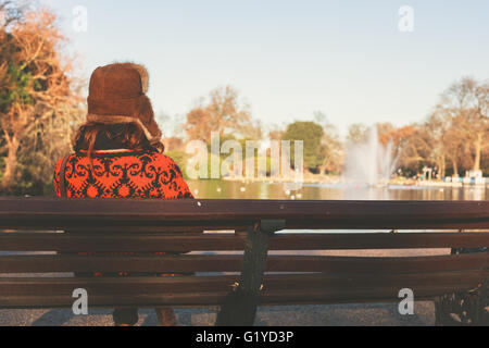 Una donna che indossa un cappello invernale è seduta su una panchina nel parco Foto Stock