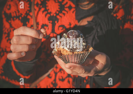 Una donna è fuori in un parco ed è in possesso di una tortina con una ciliegia Foto Stock
