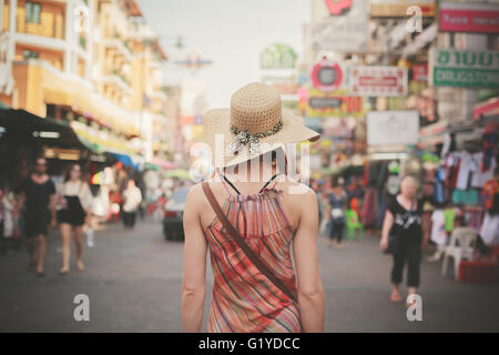 Vista posteriore di una giovane donna a piedi la famosa strada backpacker Khao San a Bangkok, in Thailandia Foto Stock