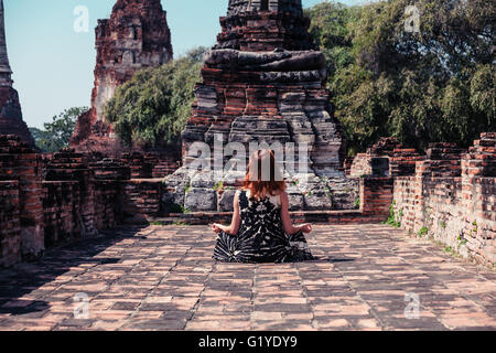 Una giovane donna è seduta e meditando tra le rovine di un antico tempio buddista Foto Stock