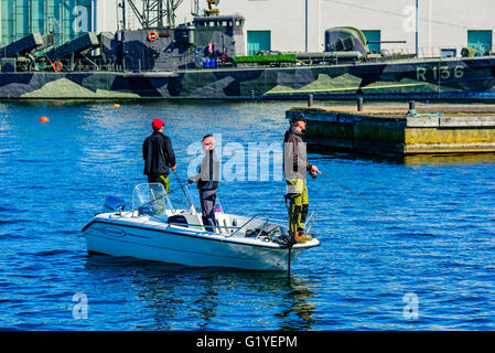 Karlskrona, Svezia - 5 Maggio 2016: tre giovani uomini adulti stand in una mezzaluna motoscafo da pesca con asta e affrontare nel porto. Foto Stock