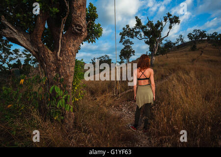 Una giovane donna è in piedi accanto a una corda pendente da un albero su una collina Foto Stock