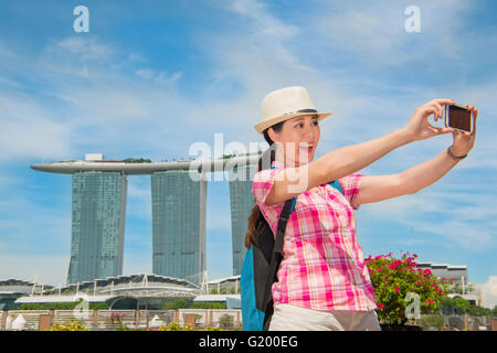 Sorridente giovane donna rendendo selfie vicino Marina Bay Sands Hotel, Singapore Foto Stock