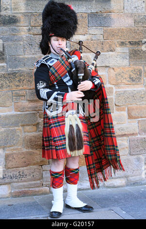 Uno scozzese che indossa il vestito tradizionale riproduzione di cornamuse al di fuori al di fuori del Castello di Edimburgo lungo la Royal Mile Foto Stock