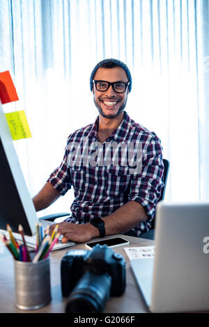Ritratto di hipster fotografo sorridente in telecamera mentre è seduto alla scrivania Foto Stock