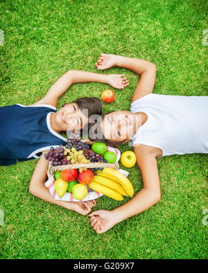 Due lieti teen boys sdraiato su un fresco e verde campo di erba, migliori amici godendo picnic all'aperto Foto Stock