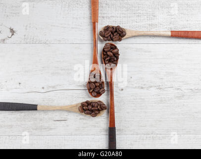 Quattro cucchiai di legno con chicchi di caffè tostati disposti in modo creativo su bianco legno rustico. Vista da sopra con lo spazio di copia Foto Stock