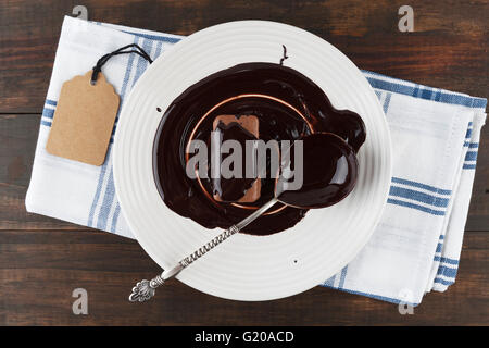 Cookie e vintage cucchiaio d'argento ricoperto di cioccolato fondente fuso su una piastra bianca e tavolo in legno con tag regalo. Foto Stock