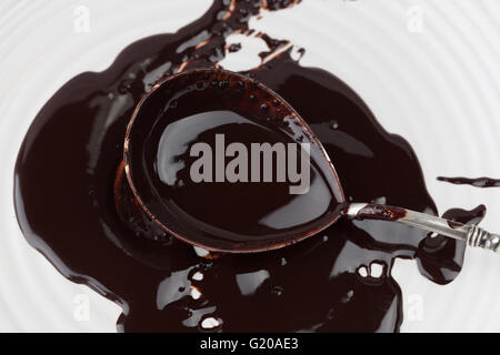 Primo piano di vintage cucchiaio d'argento riempita con dark cioccolato fuso sulla piastra bianca Foto Stock