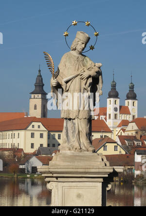 Statua in marmo di San Giovanni croce di contenimento e piuma penna con Telc torri in background, Southwestern Moravia Repubblica Ceca Foto Stock