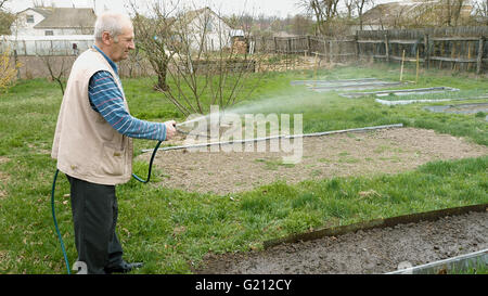 Senior uomo anziano acque un letto orto Foto Stock