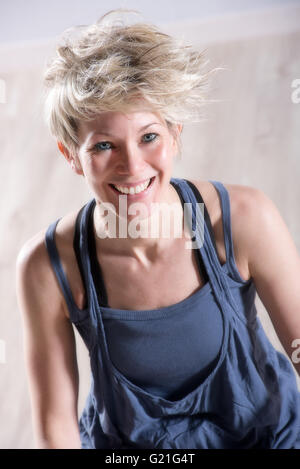 Ritratto di atletica unico bella donna bionda in abito blu ridendo e guardando in avanti sopra la pietra Sfondo marmo Foto Stock