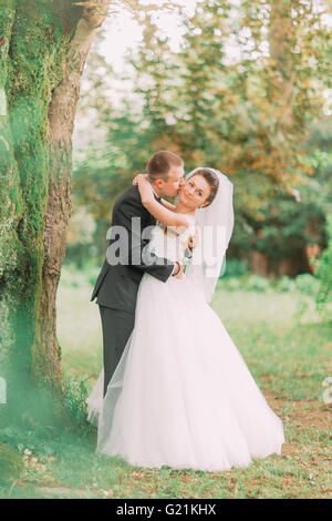 Lo sposo baci una guancia di felice sposa vicino autumn tree in posizione di parcheggio Foto Stock