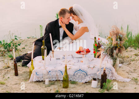 Giovani coppie in viaggio di nozze che abbraccia in serata romantica con candele sulla spiaggia di sabbia Foto Stock