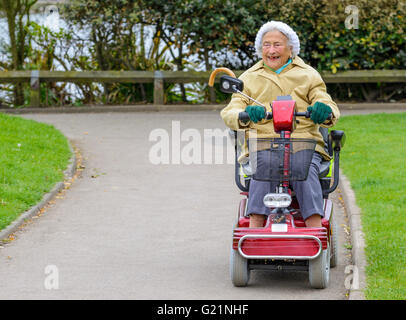 Felice signora anziana a cavallo di un scooter di mobilità in un parco. Foto Stock