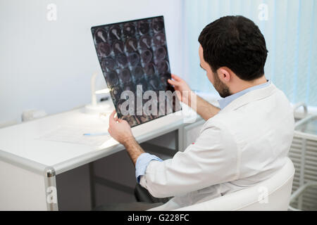 Giovane maschio medico di leggere e rivedere un cervello MRI scan Foto Stock