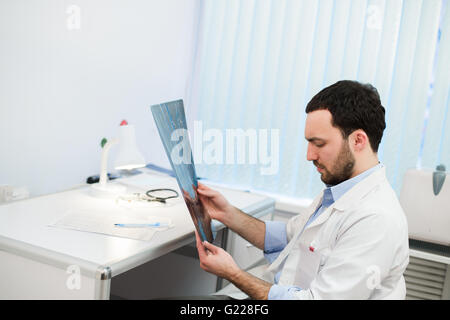 Giovane uomo caucasico medico esamina l'immagine MRI della testa umana in office Foto Stock